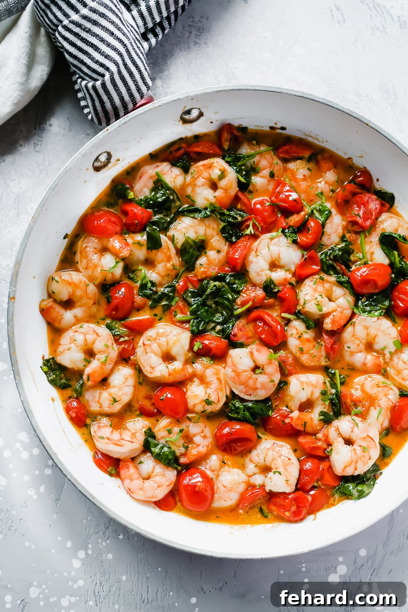 Parmesan Shrimp Perfection 2 Overhead view of a white pan with creamy parmesan shrimp with greens and tomatoes.