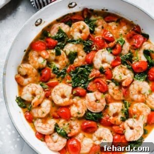 Overhead view of a white pan with creamy parmesan shrimp with greens and tomatoes.