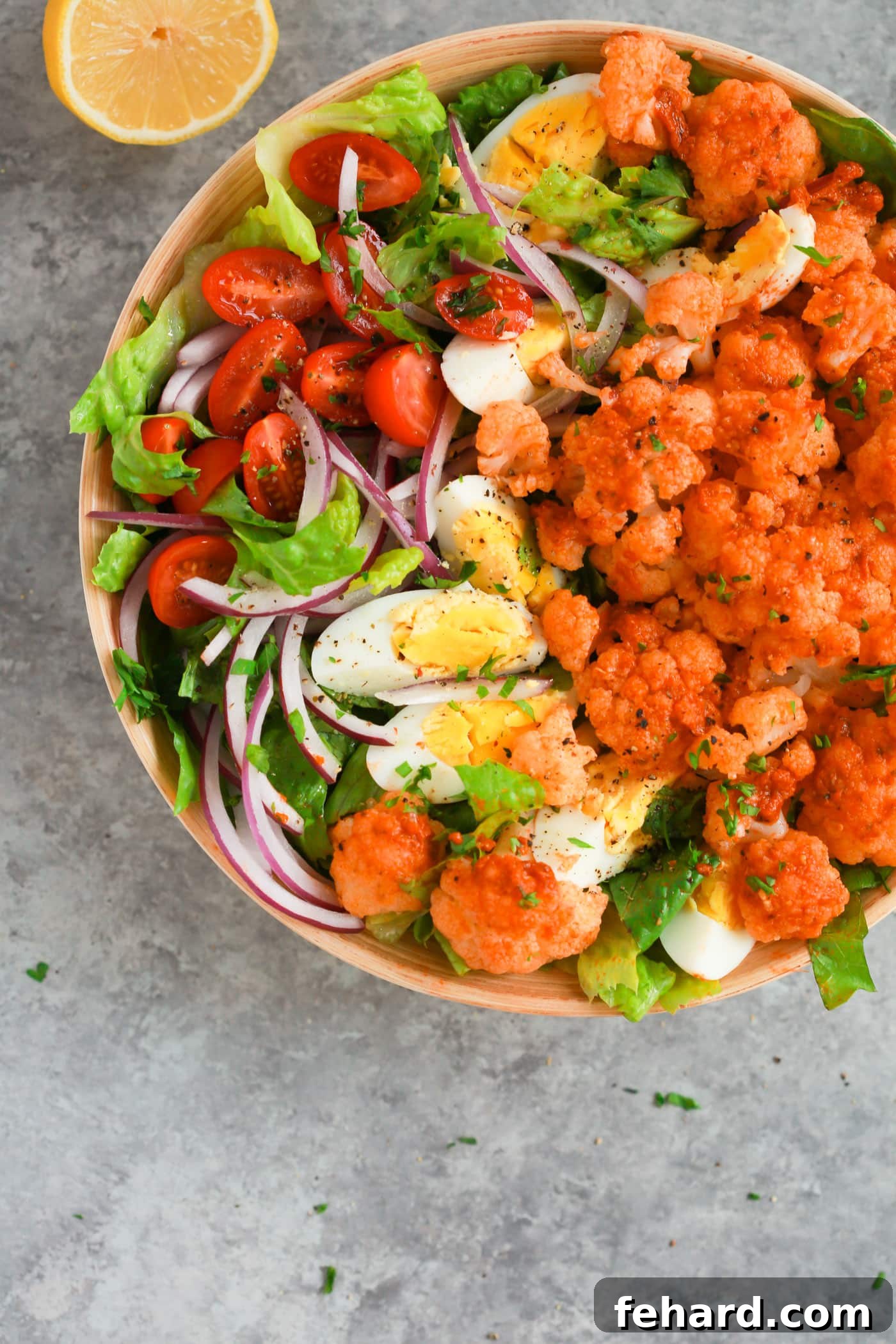 Overhead view of a sun-dried tomato pesto cauliflower salad in a rustic wooden bowl.