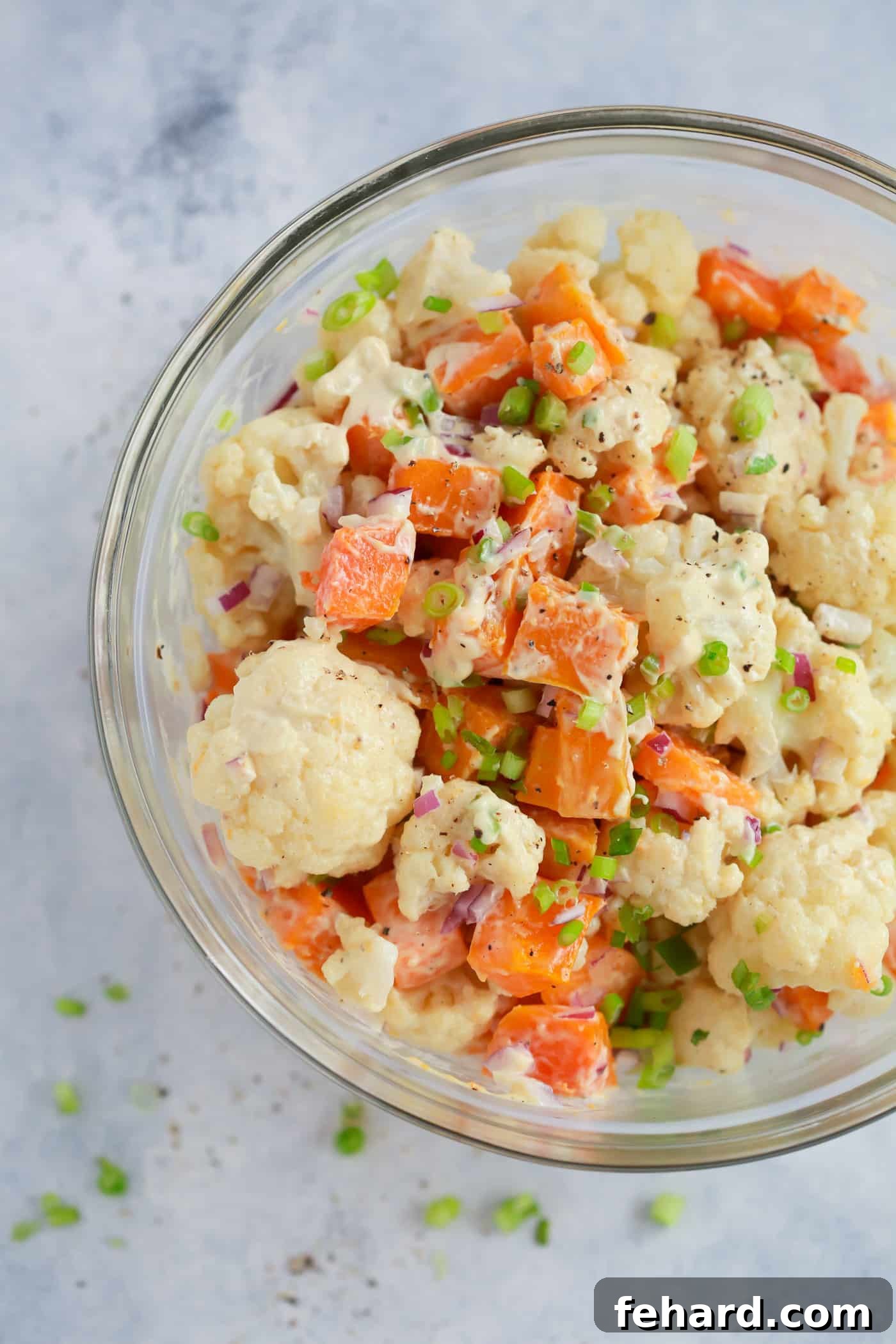 Overhead view of a hearty roasted butternut squash and cauliflower salad in a clear glass bowl.