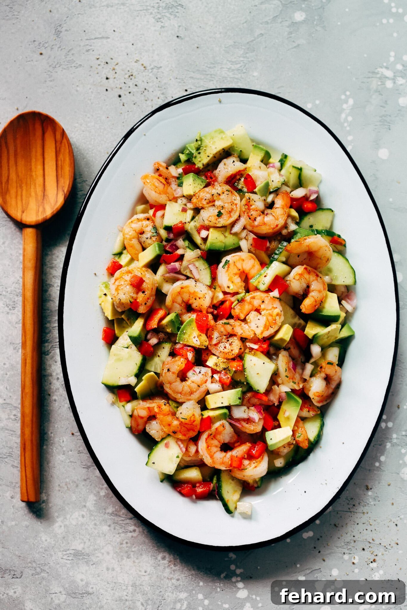 An oval serving platter presenting a colorful shrimp, avocado, and cucumber salad.