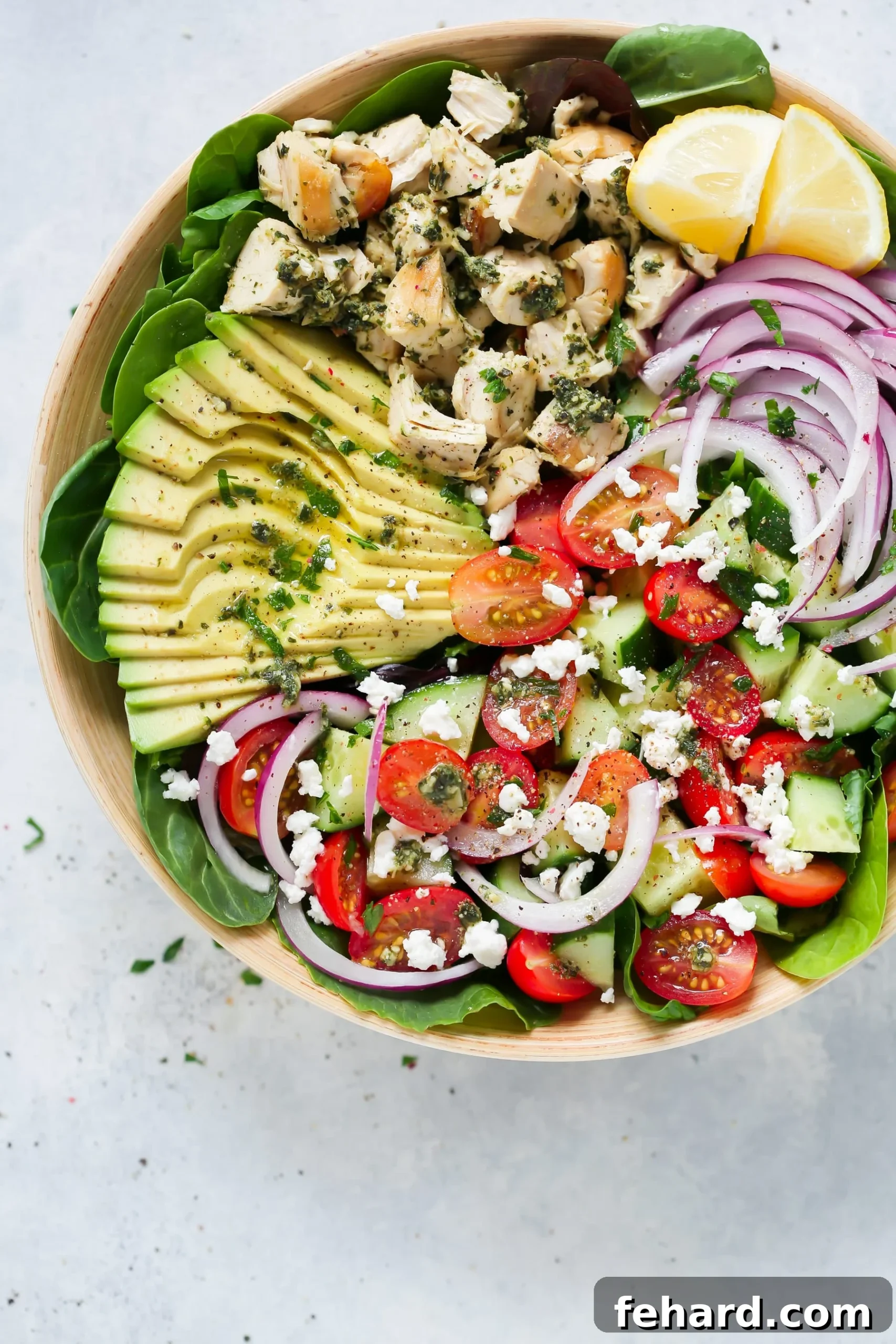 Overhead view of a vibrant pesto chicken salad in a wooden bowl, garnished with fresh basil leaves.