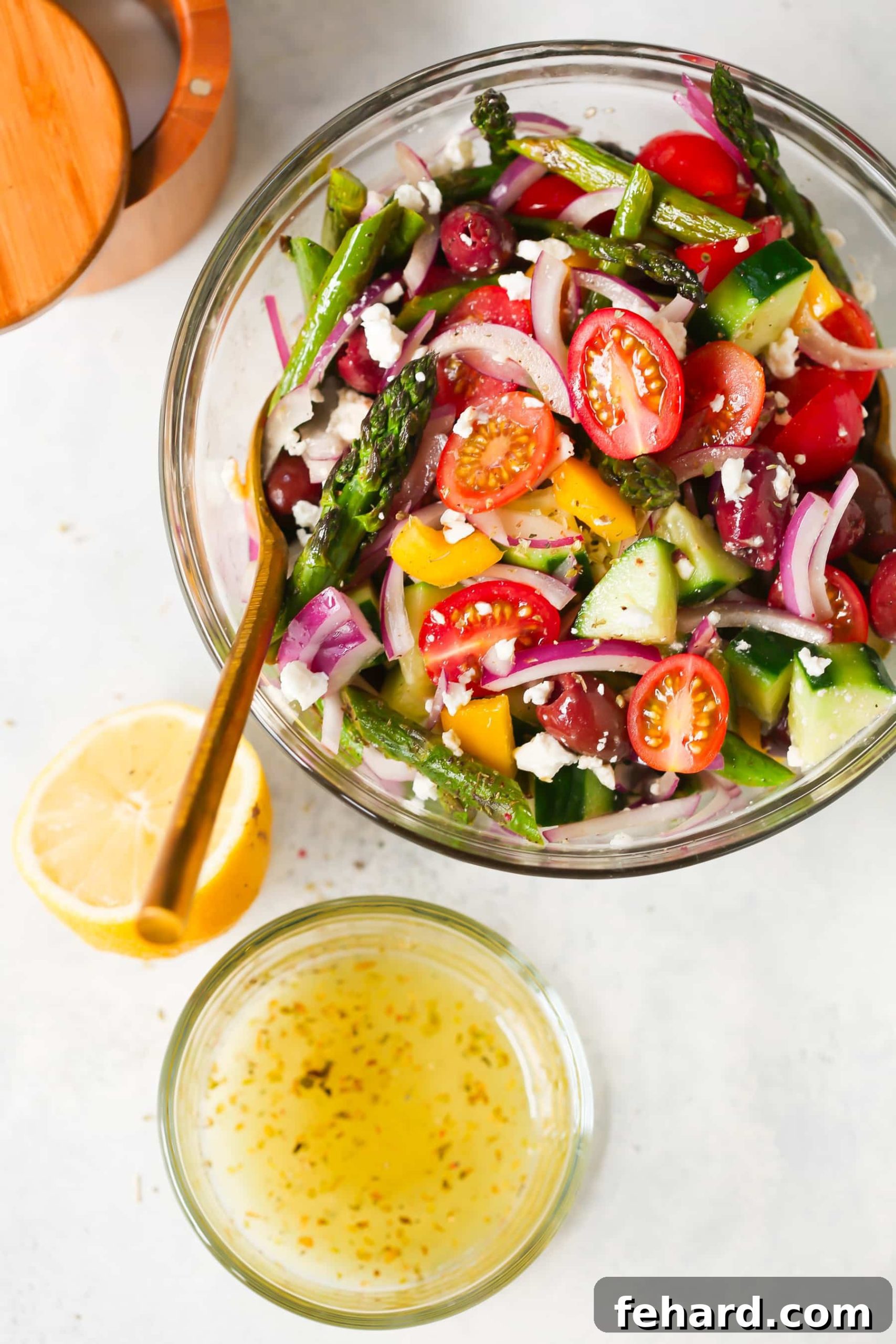 Overhead view of an vibrant asparagus Greek chopped salad in a clear glass bowl, showcasing fresh ingredients.