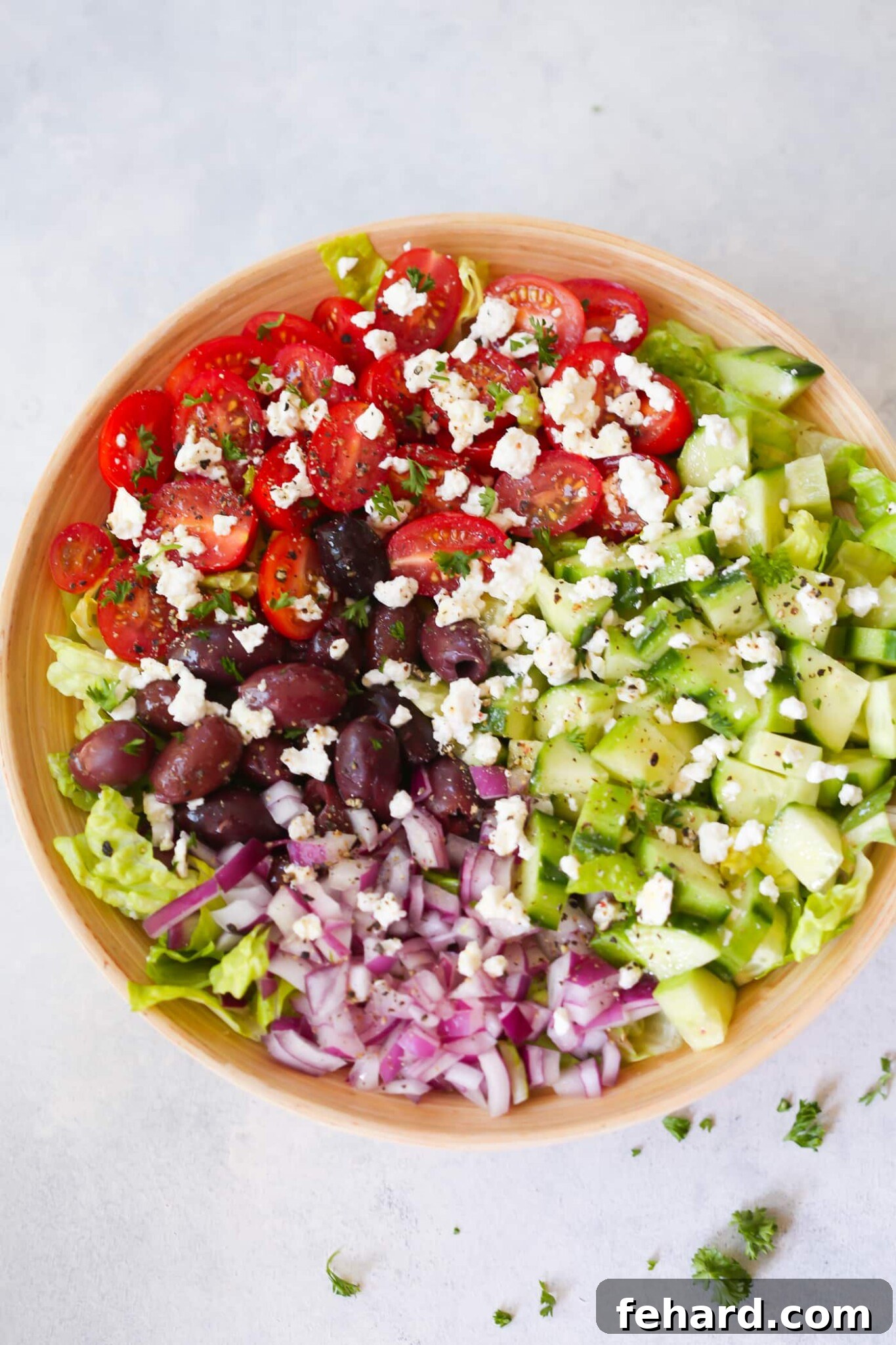 Overhead view of a colorful Mediterranean chopped salad served in a rustic wooden bowl.