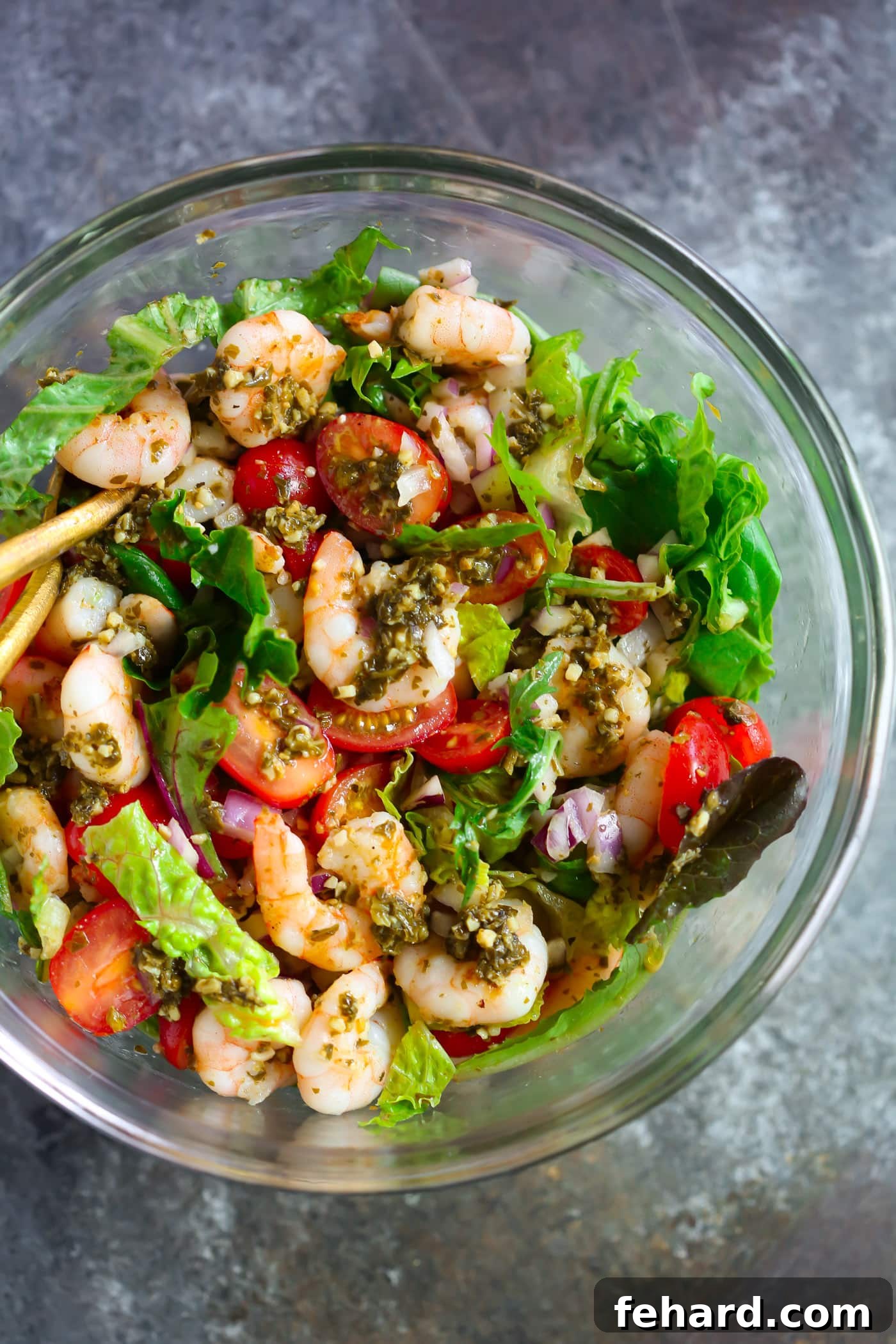 A clear glass bowl filled with vibrant pesto shrimp tomato salad, ready to be enjoyed.