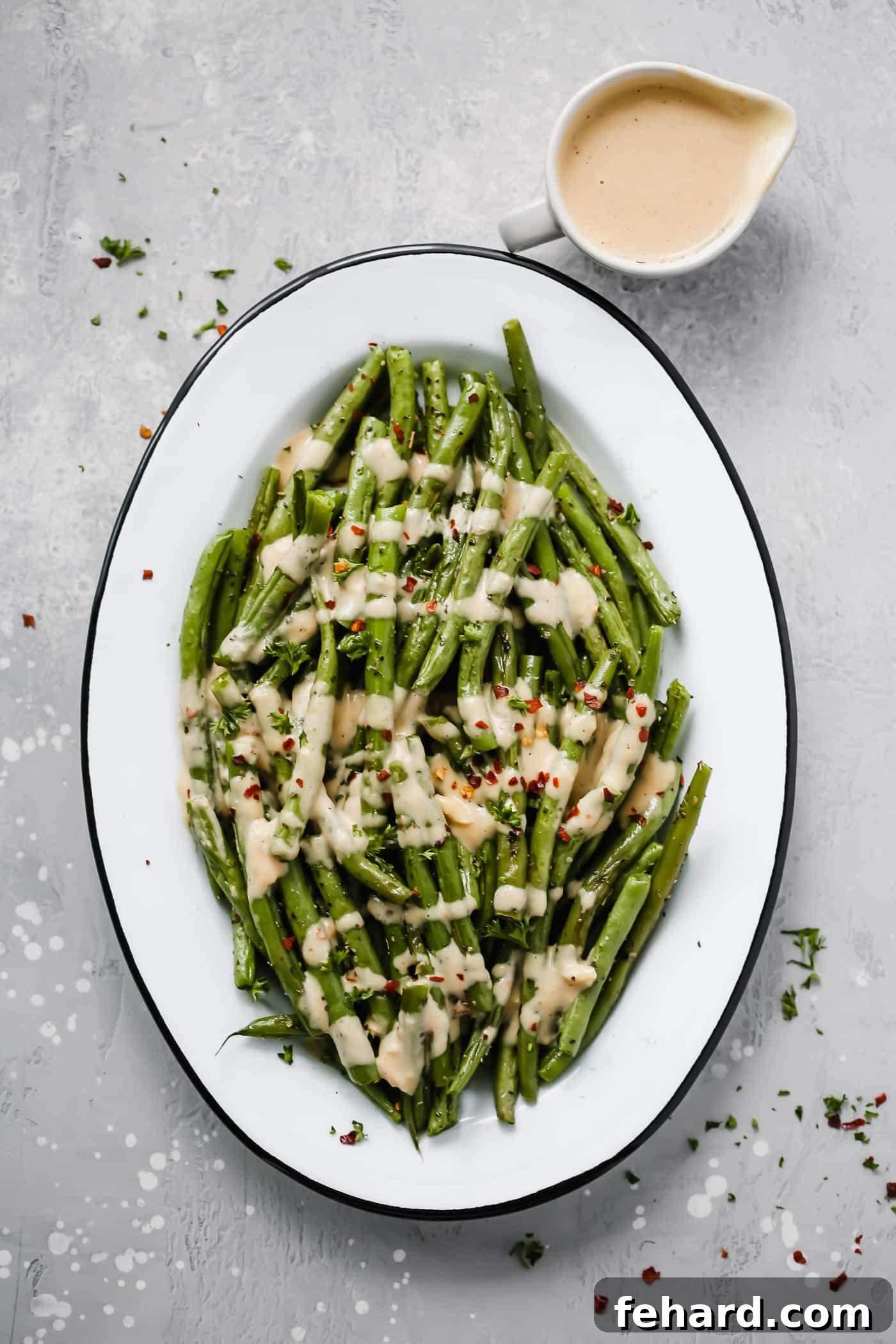 An oval serving platter with roasted green beans with spicy tahini sauce, garnished with fresh parsley.
