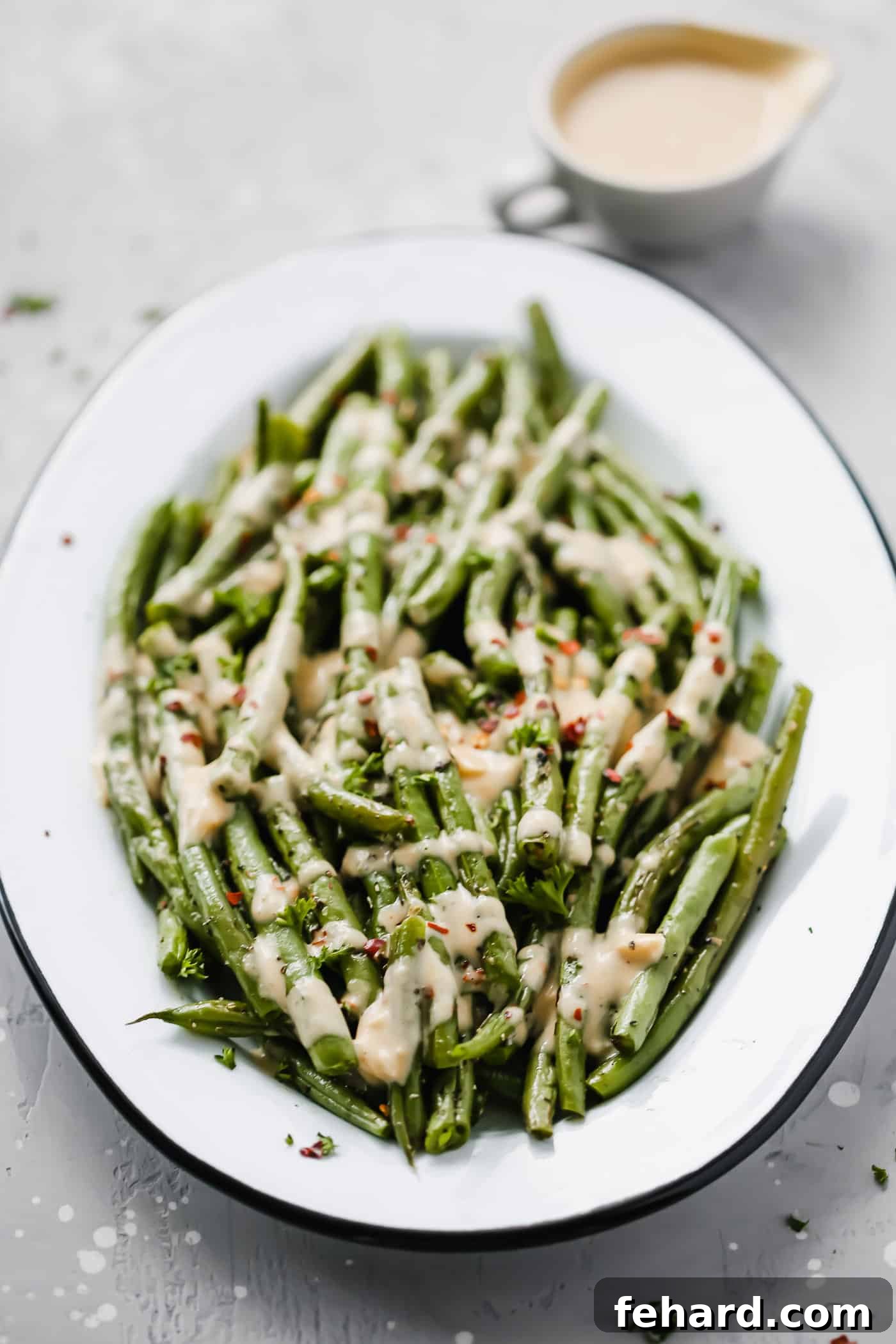 Overhead view of roasted green beans with spicy tahini sauce on a white serving plate, highlighting the vibrant colors.