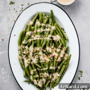 An oval serving platter with roasted green beans with spicy tahini sauce.