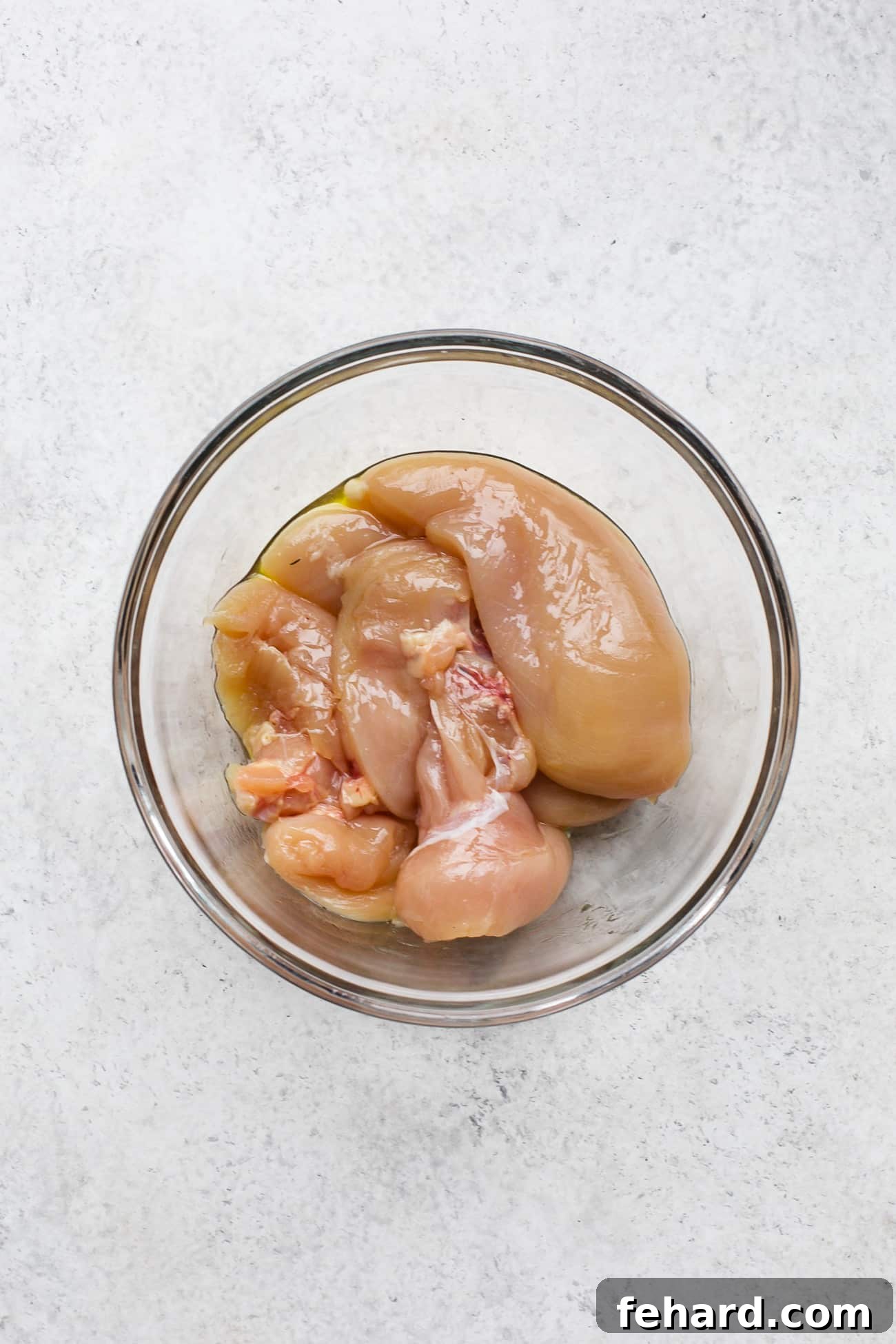 Seasoning chicken breast in a large bowl with various spices and a dash of hot sauce.