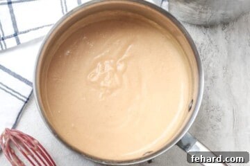 Creamy Homemade Chicken Soup 3 Creamy homemade cream of chicken soup in saucepan next to a red whisk, showing its rich texture.