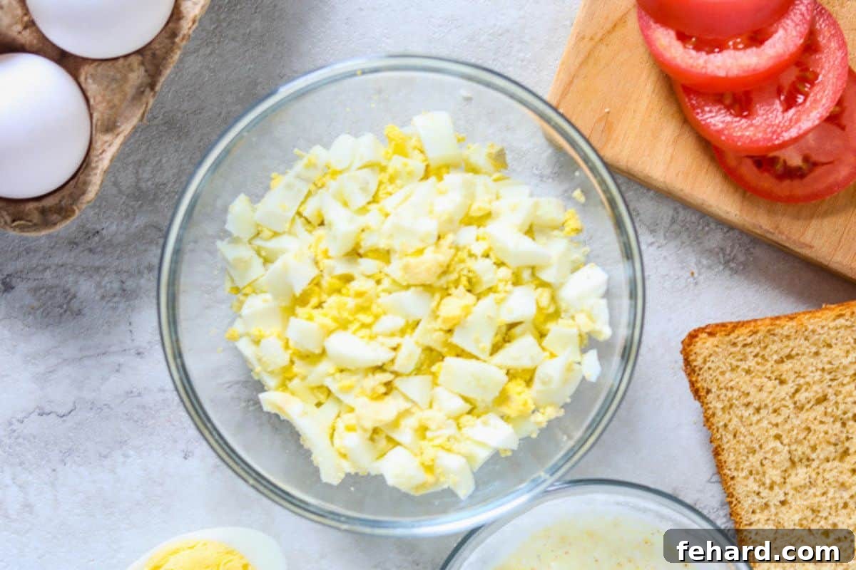 Best Easy Egg Salad Preparation Chopped hard-boiled eggs in a mixing bowl, beside a separate bowl containing the prepared dressing for egg salad.