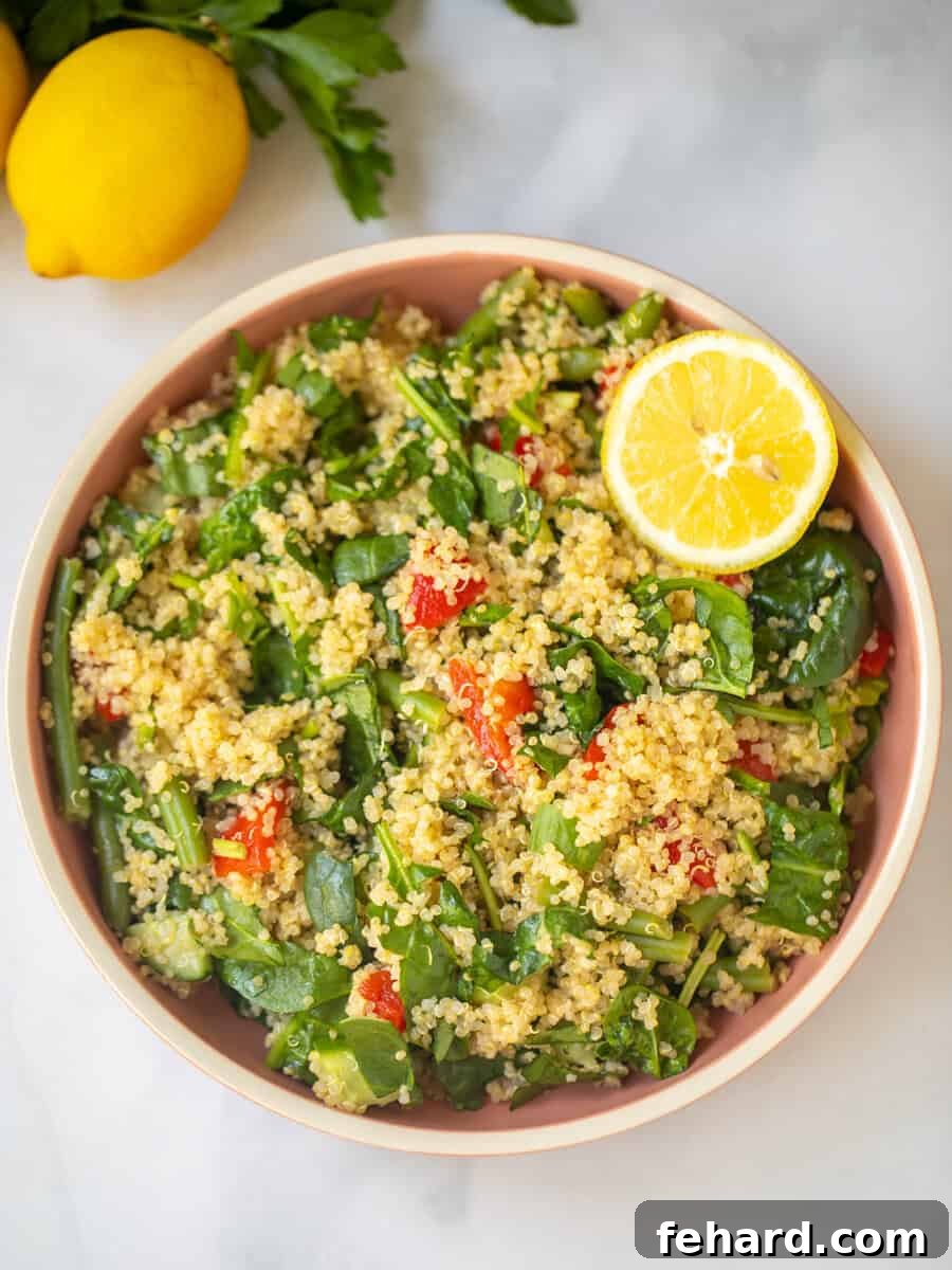 A beautifully presented bowl of Quinoa Spinach Salad, garnished with fresh lemon wedges and vibrant green beans in the background, highlighting its fresh and wholesome appeal.