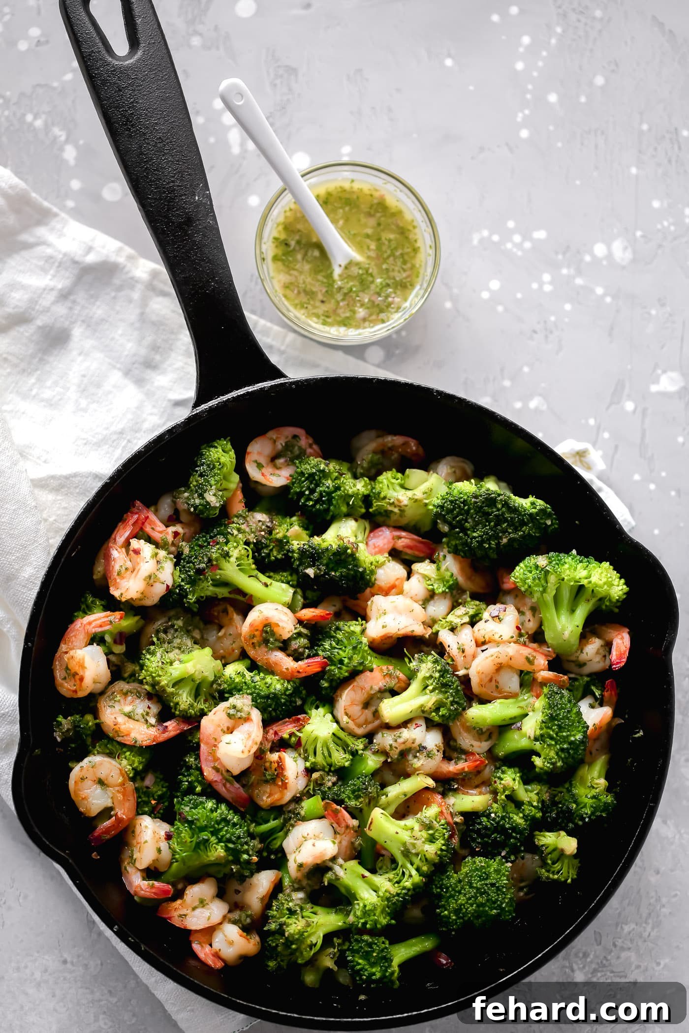 An overhead view of a rustic cast-iron skillet, showcasing plump shrimp and tender broccoli florets, glistening with a savory sauce.