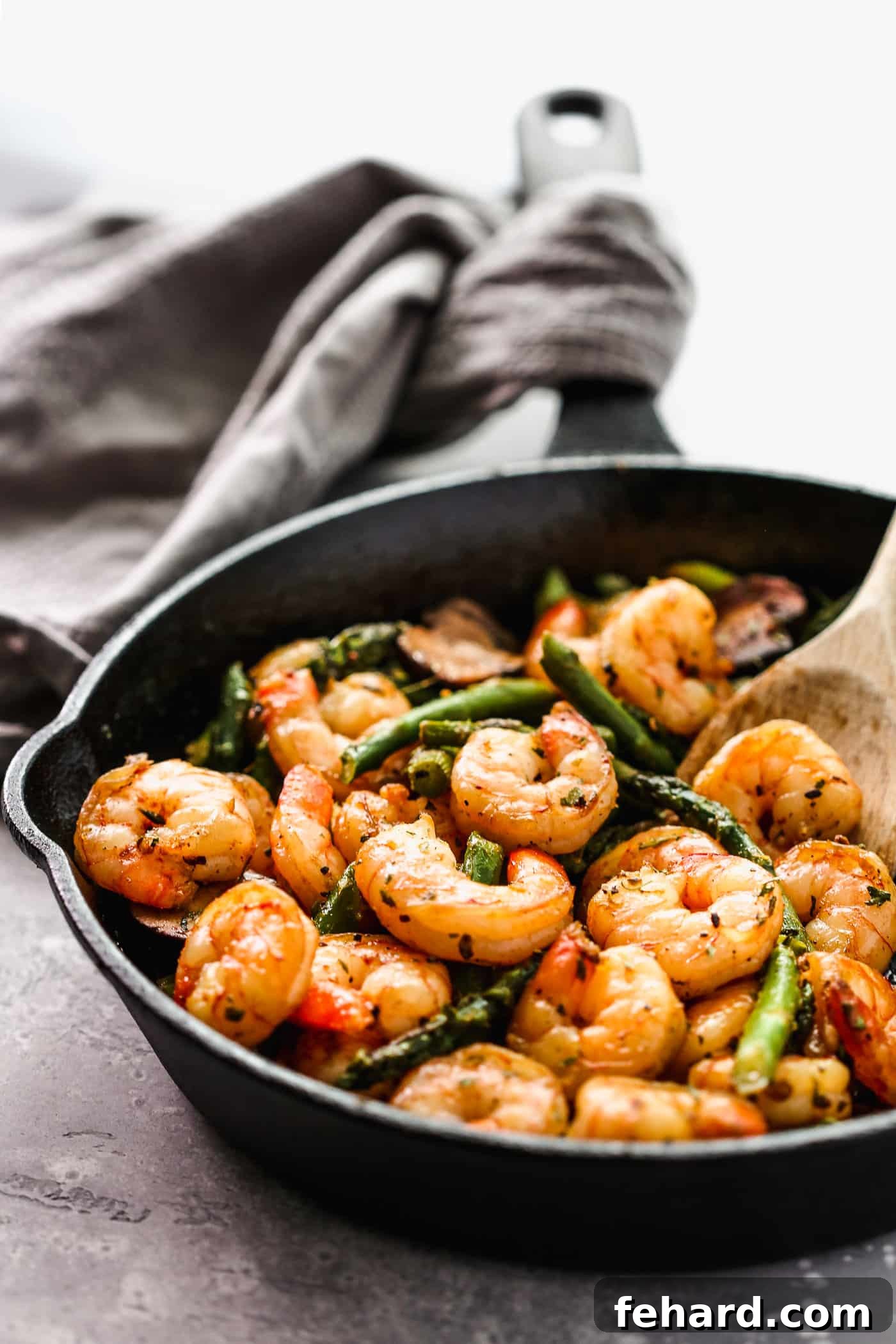 Sizzling shrimp and tender asparagus spears elegantly arranged in a cast-iron skillet, accompanied by a rustic wooden spoon.