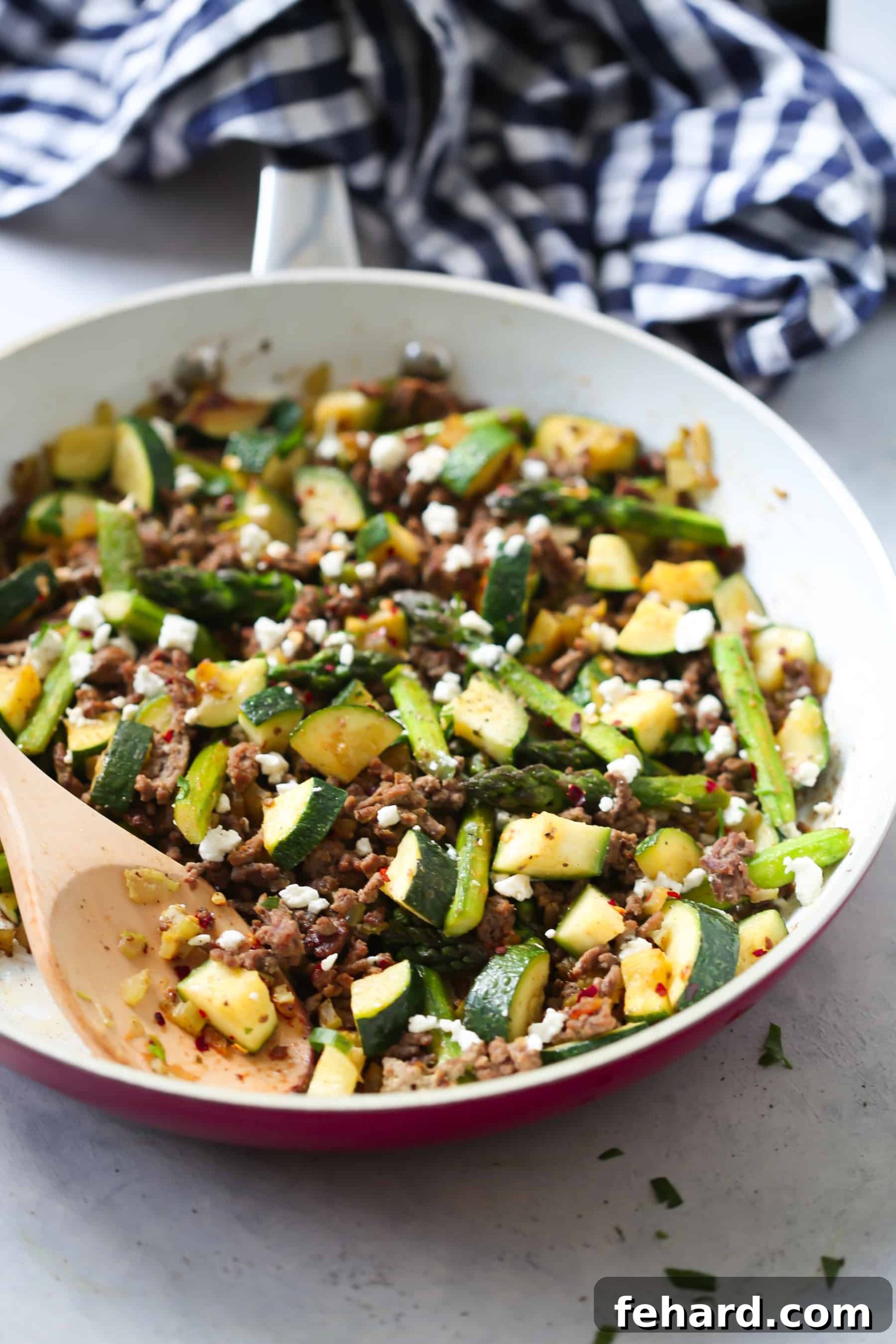 A vibrant ground beef veggie skillet in a pristine white pan, with a wooden spoon gently stirring the medley of fresh ingredients.