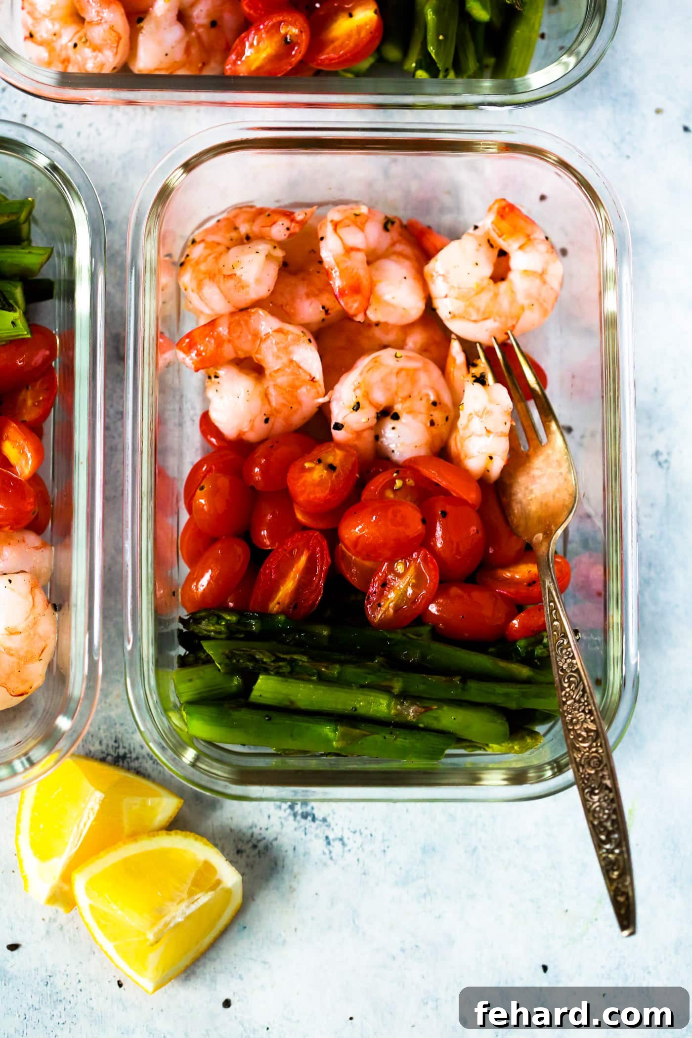 Several meal prep containers neatly arranged, each brimming with perfectly cooked shrimp, sweet cherry tomatoes, and crisp asparagus, with a fork poised for enjoyment.