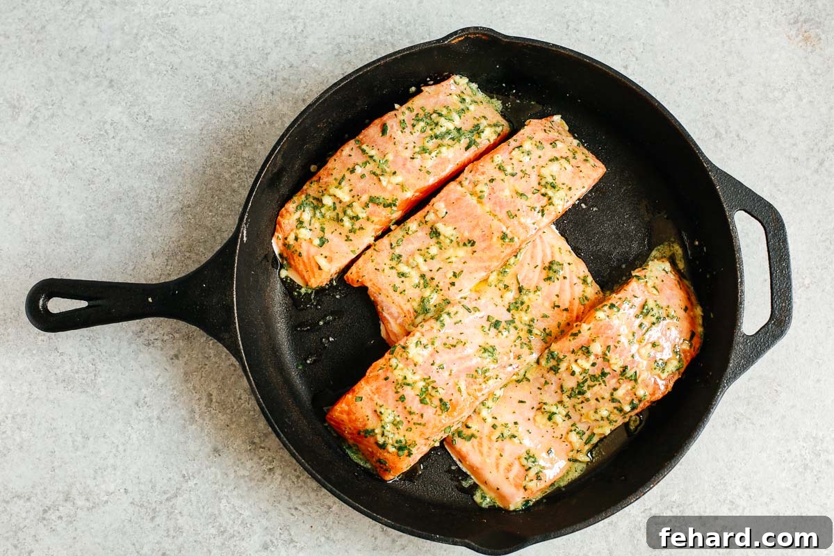 Cast iron skillet with raw salmon fillets generously coated in the Dijon mustard sauce, ready for baking.