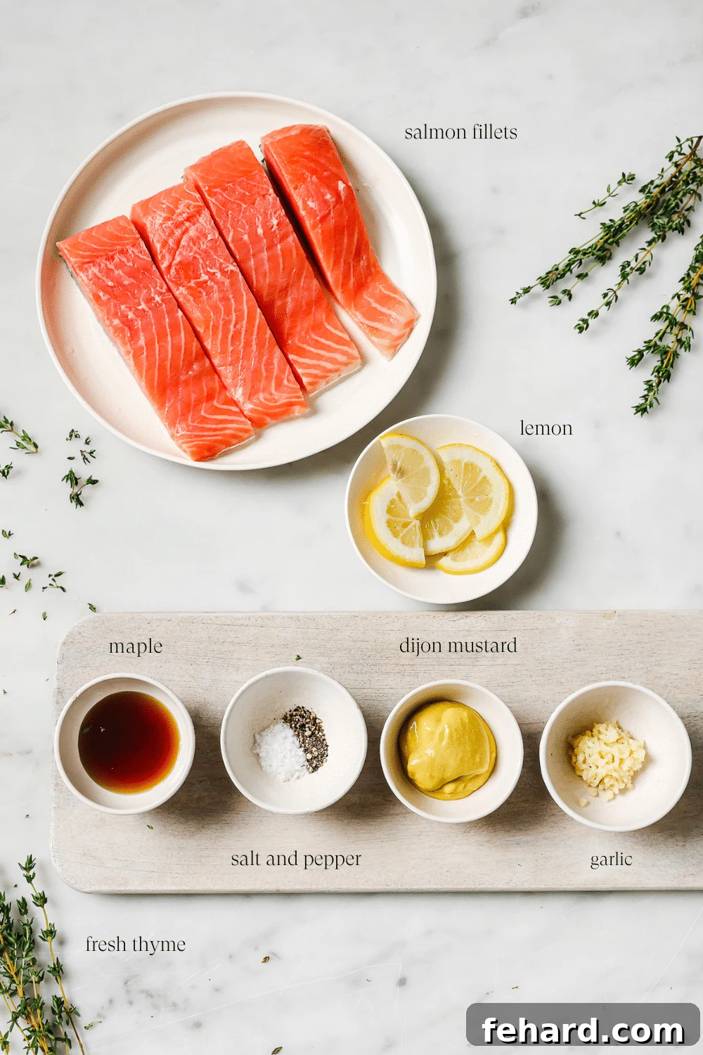 Maple Mustard Glazed Salmon 3 Pre-measured ingredients in small bowls on a cutting board and white countertop, including salmon, maple syrup, Dijon mustard, garlic, and thyme.