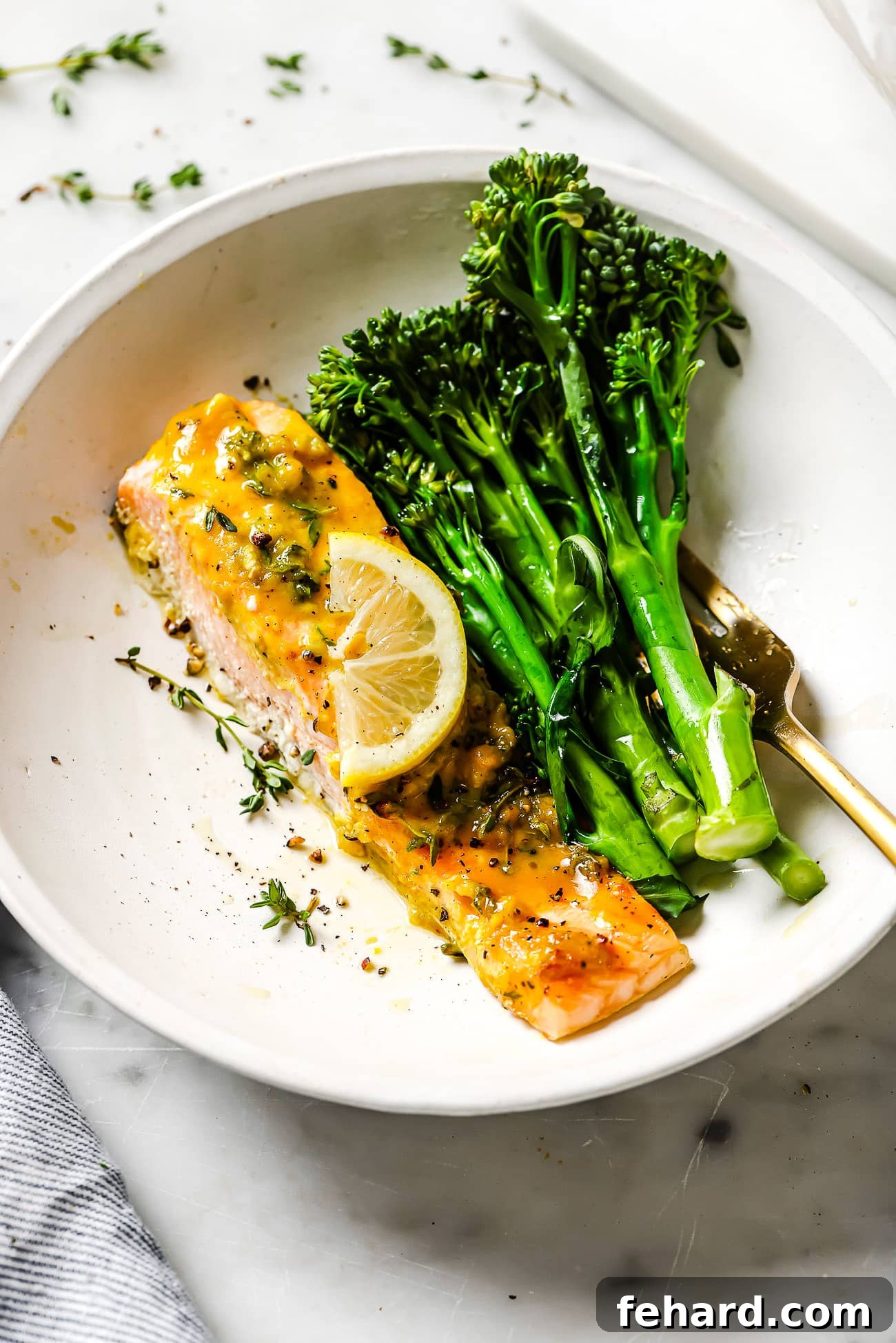 Maple Mustard Glazed Salmon 6 Maple mustard salmon on a white plate with broccolini, garnished with lemon and fresh herbs.