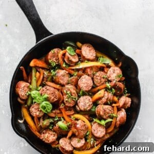 Overhead view of a cast iron skillet containing cooked Italian sausage and bell peppers, garnished with fresh herbs.