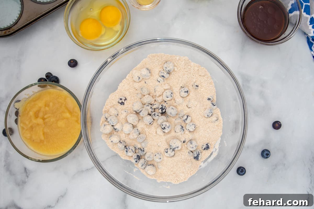 No Sugar Added Blueberry Muffins Whole wheat flour lightly tossed with fresh blueberries in a mixing bowl, ready for wet ingredients.