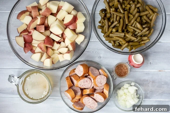 Smoked Sausage and Potatoes with Green Beans Ingredients A flat lay of the key ingredients: whole red potatoes, fresh green beans, smoked sausage links, a small bowl of Cajun seasoning, and a carton of chicken stock, all arranged on a white kitchen counter.