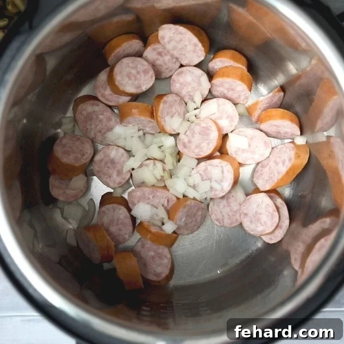 Sautéing Smoked Sausage and Onions in Instant Pot Sliced smoked sausage and minced onions sizzling and browning in the inner pot of an Instant Pot during the sautéing process.