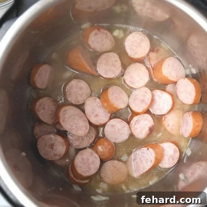 Deglazing Instant Pot with Chicken Stock Chicken stock being poured over the sautéed smoked sausage in the Instant Pot, with a spoon scraping the bottom to deglaze.