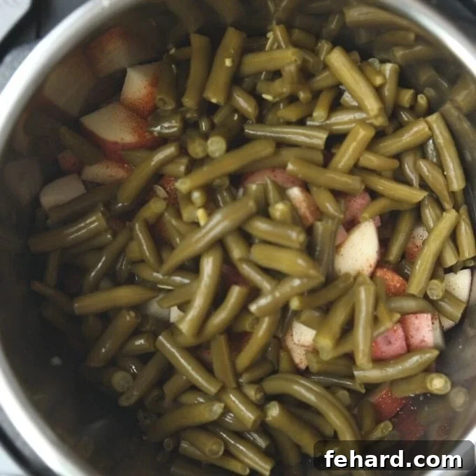 Layering Ingredients for Instant Pot Smoked Sausage Cubed potatoes, Cajun seasoning, and drained green beans layered over the sausage and stock in the Instant Pot, ready for pressure cooking.