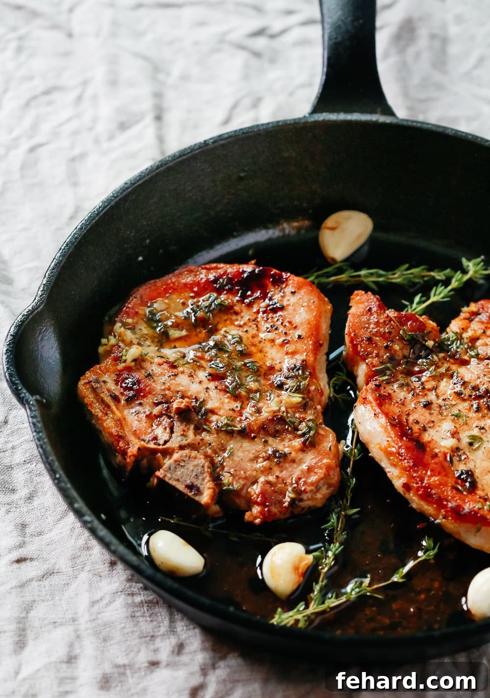 overhead view of Garlic Butter Baked Pork Chops in a cast iron skillet, golden brown and garnished with fresh herbs