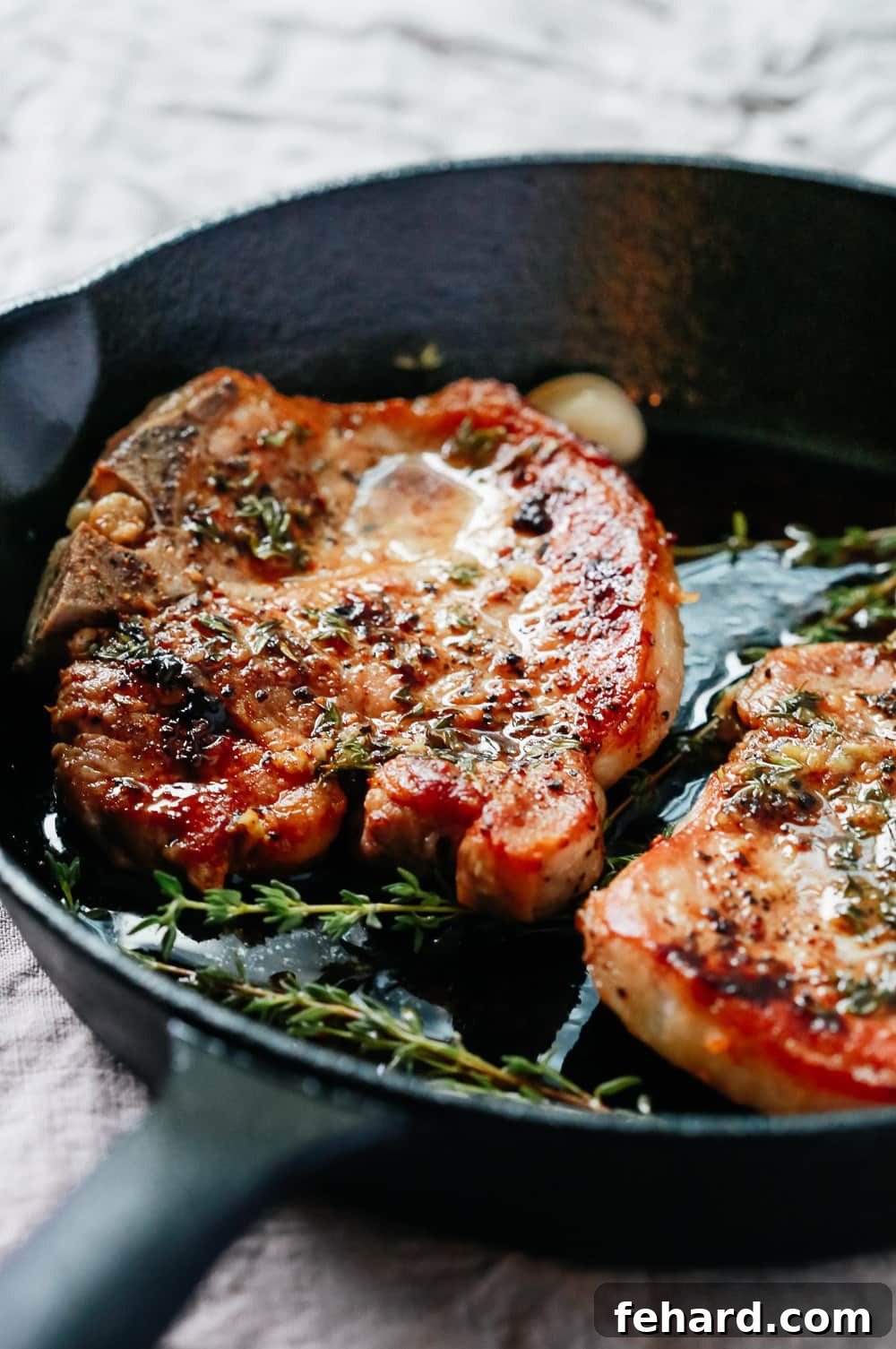 CLose-up view of the baked pork chops in a cast iron skillet, showing the golden crust and garlic butter sauce