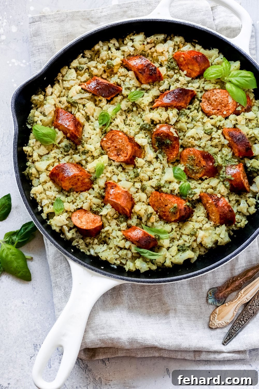 Italian Sausage Cauliflower Rice Skillet with pesto and basil leaves on top