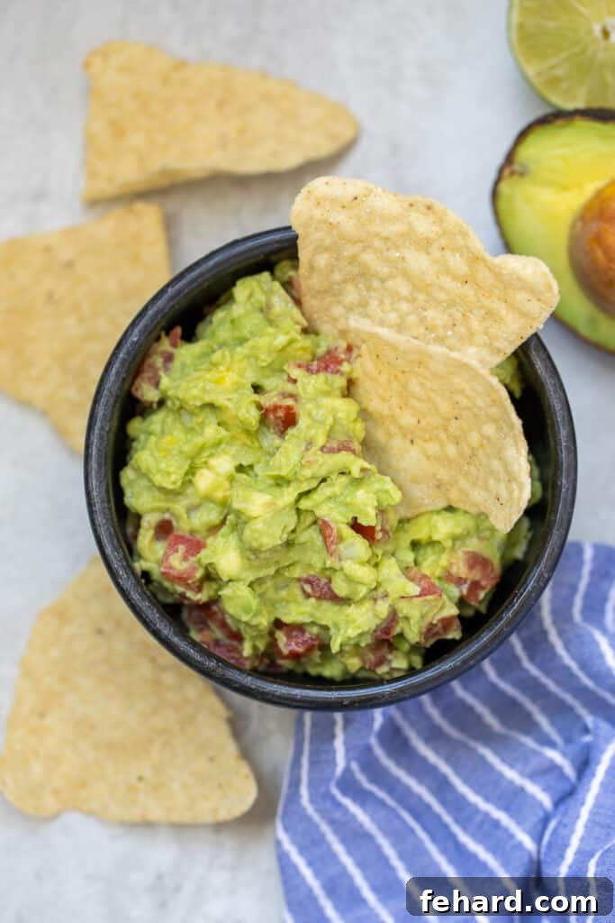 Homemade Guacamole A vibrant bowl of homemade chunky guacamole, garnished with fresh tomatoes and served with a side of crispy tortilla chips.