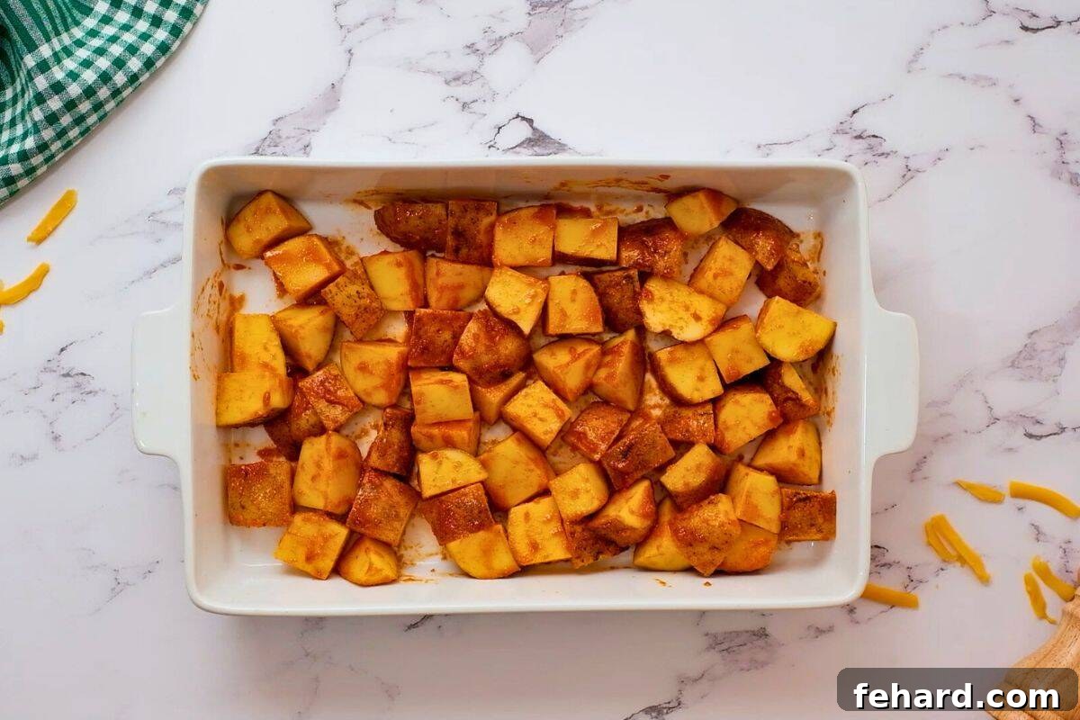 Cubed russet potatoes seasoned with buffalo spices and olive oil, spread evenly in a white casserole dish ready for roasting.