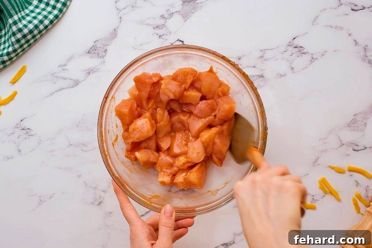 Cubed chicken breasts being tossed in a mixing bowl with hot sauce and buffalo wing seasonings, absorbing flavors.