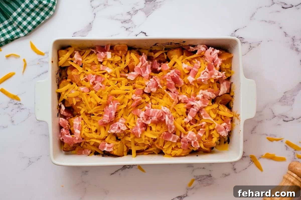 Layers of roasted potatoes, seasoned raw chicken, diced bacon, and shredded cheddar cheese assembled in a white casserole dish, ready for baking.
