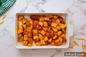 Potatoes seasoned with buffalo seasonings spread out in a white casserole dish, ready for roasting.