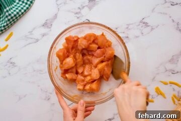 Cubed chicken breasts in mixing bowl being tossed with hot sauce and buffalo wing seasonings, preparing for the casserole.