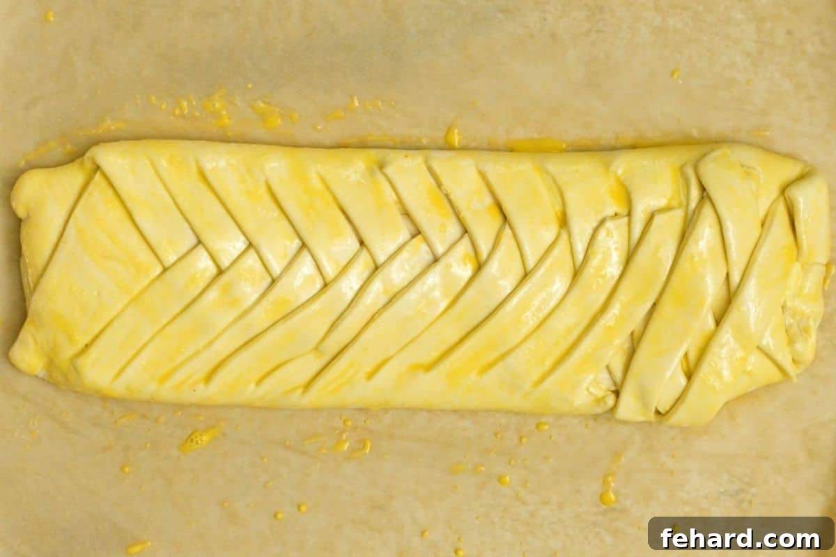 A beautifully braided cream cheese danish on parchment paper, glistening with an egg wash, ready for baking.