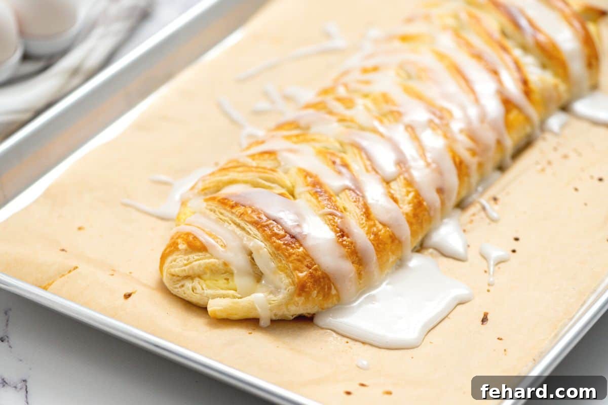 A beautifully glazed puff pastry cream cheese danish resting on a baking sheet, with the lemon glaze visibly set and shimmering.