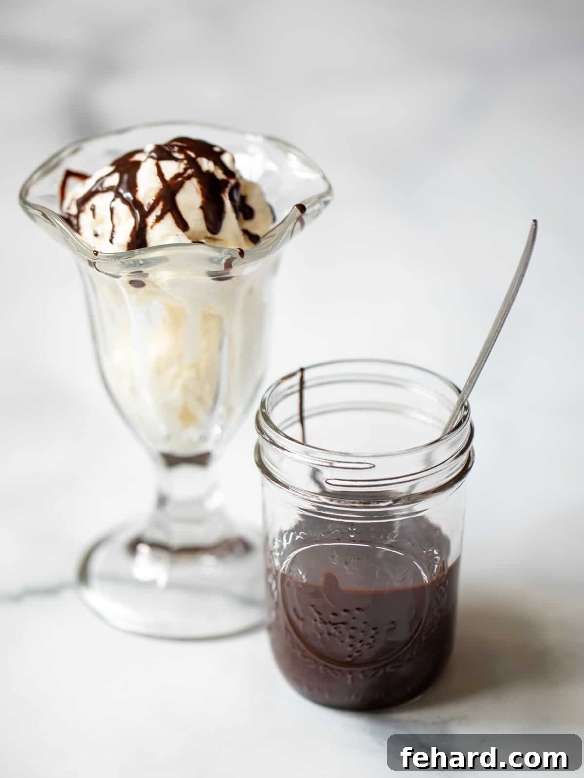 A jar of rich, dark homemade chocolate syrup perfectly positioned next to a tempting vanilla ice cream sundae, highlighting its versatility as a dessert topping.