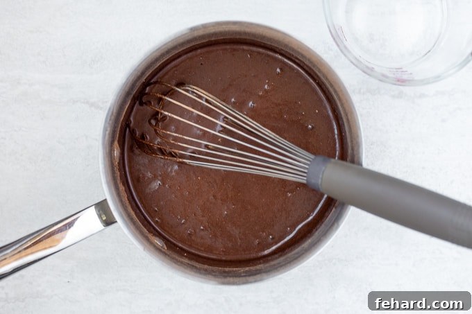A small saucepan on a stove, containing the chocolate syrup mixture, with a whisk actively stirring it to prevent lumps and ensure smoothness.