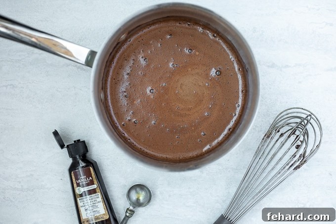 A saucepan of finished homemade chocolate syrup, appearing rich and glossy, after the final flavorings have been stirred in.