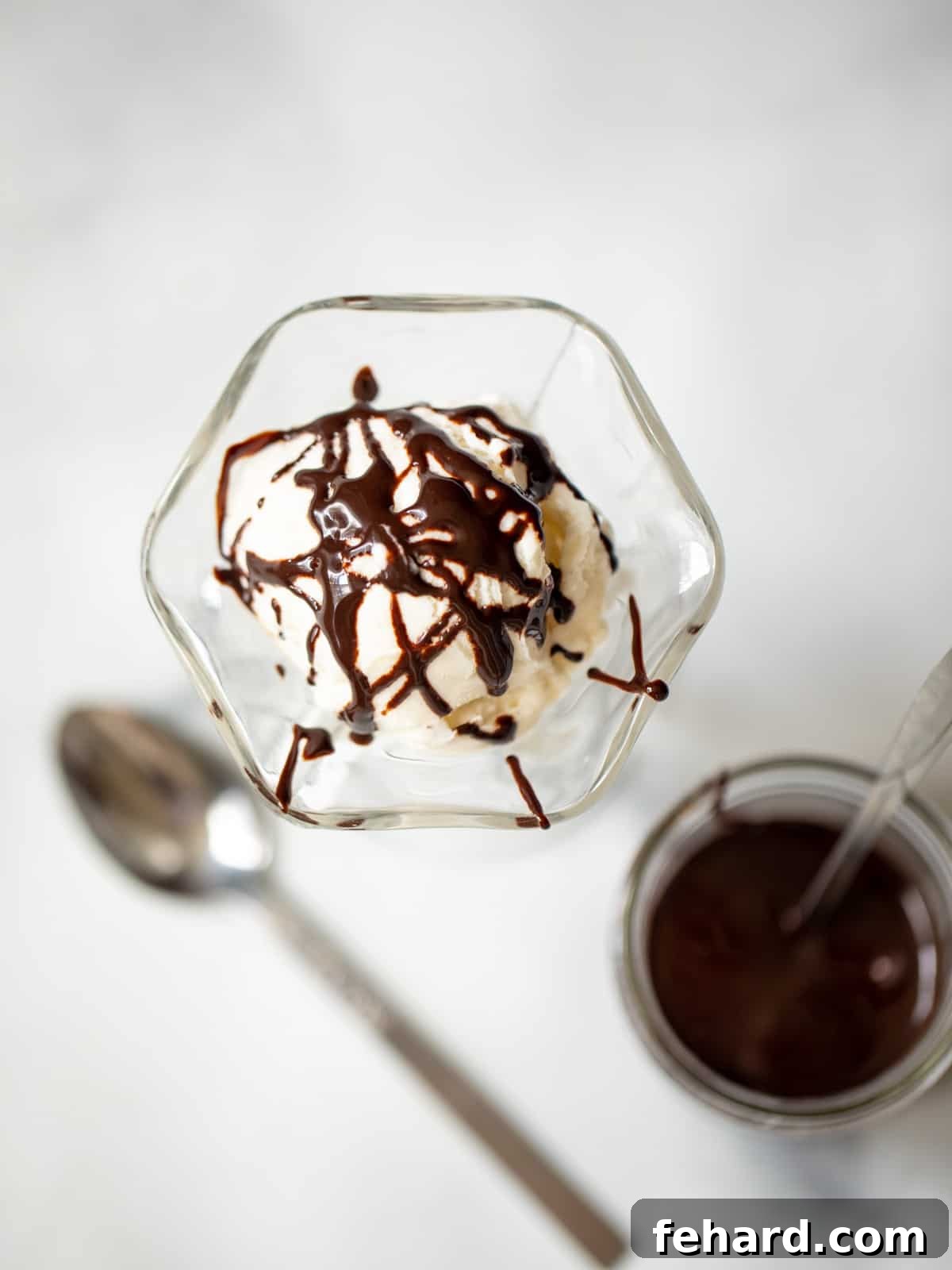 A perfectly prepared jar of dairy-free homemade chocolate syrup, artfully placed beside a scoop of creamy vanilla ice cream, signifying its readiness for enjoyment.
