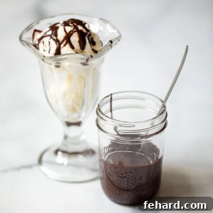 A charming glass jar of homemade chocolate syrup resting beside a classic vanilla ice cream sundae, ready for drizzling.
