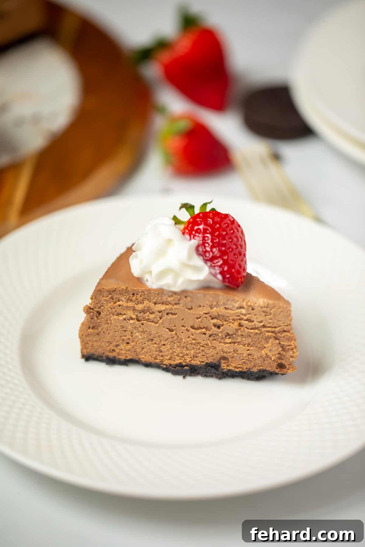 Instant Pot Chocolate Cheesecake A perfectly sliced piece of Instant Pot chocolate cheesecake on a white plate, adorned with a dollop of whipped cream and a fresh strawberry.