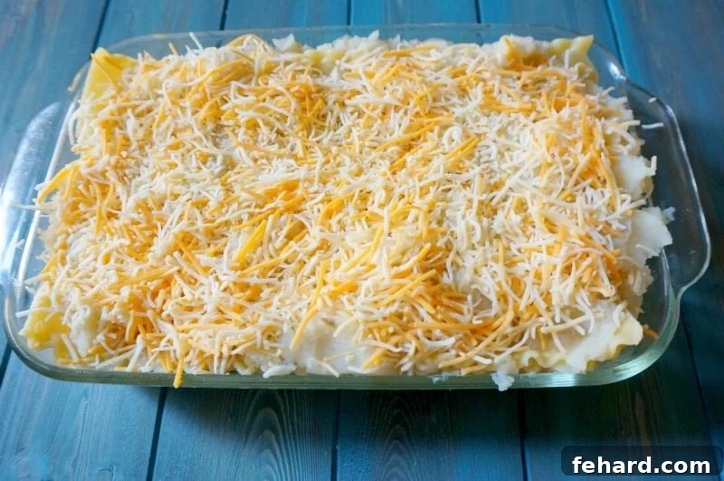 An unbaked Pierogi Lasagna in a glass baking dish, topped with cheese and bacon, ready for the oven.