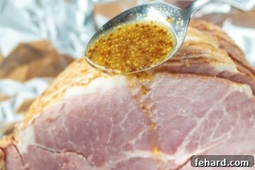 Spoon pouring pineapple mustard glaze over ham.