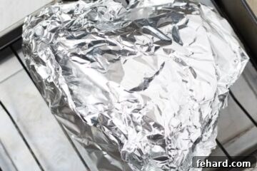 Ham wrapped in foil on roasting rack in roasting pan with water before baking.