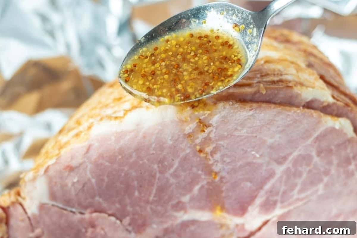 A spoon gracefully pouring the rich, golden pineapple Dijon mustard glaze over a spiral-sliced ham, allowing the glaze to coat every crevice and infuse flavor.